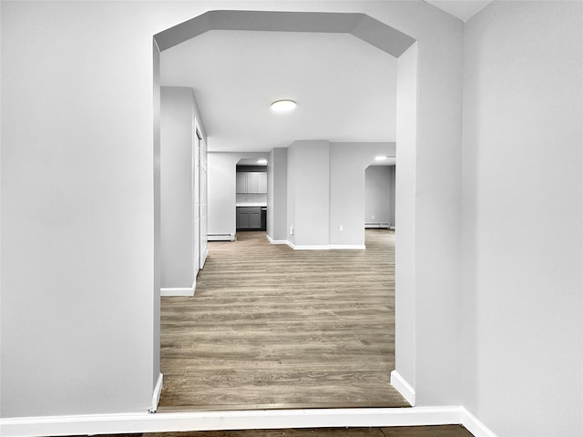 corridor with wood-type flooring and a baseboard heating unit