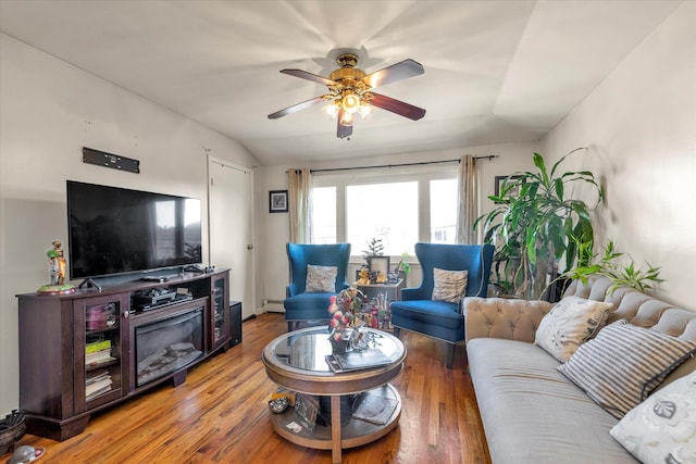 living room with baseboard heating, ceiling fan, wood-type flooring, and vaulted ceiling