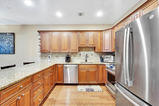 kitchen featuring light stone counters, sink, light hardwood / wood-style flooring, and appliances with stainless steel finishes