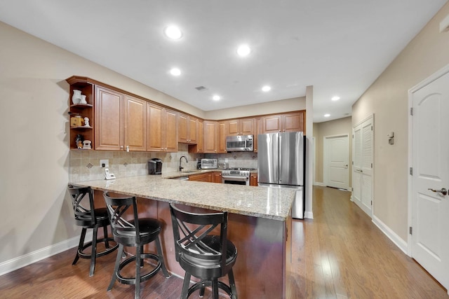 kitchen with kitchen peninsula, light hardwood / wood-style floors, a breakfast bar area, decorative backsplash, and appliances with stainless steel finishes