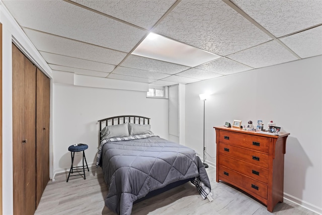 bedroom with a closet, light hardwood / wood-style floors, and a drop ceiling