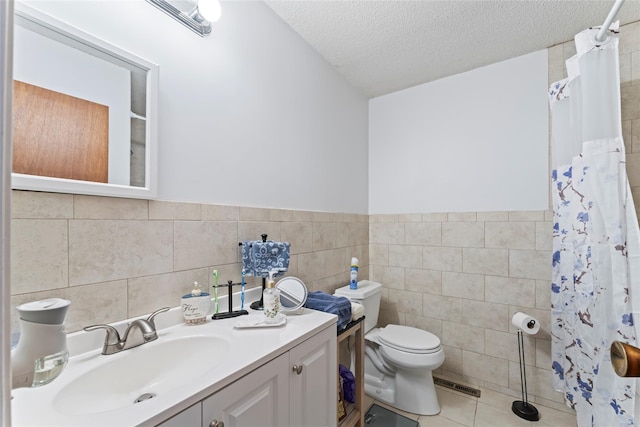 bathroom with vanity, tile patterned floors, toilet, a textured ceiling, and tile walls