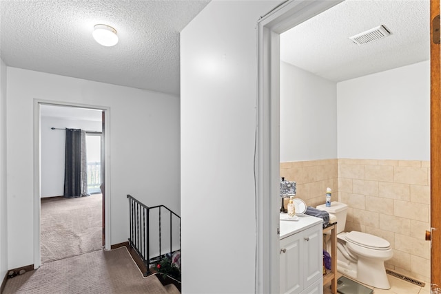 bathroom featuring a textured ceiling, vanity, toilet, and tile walls