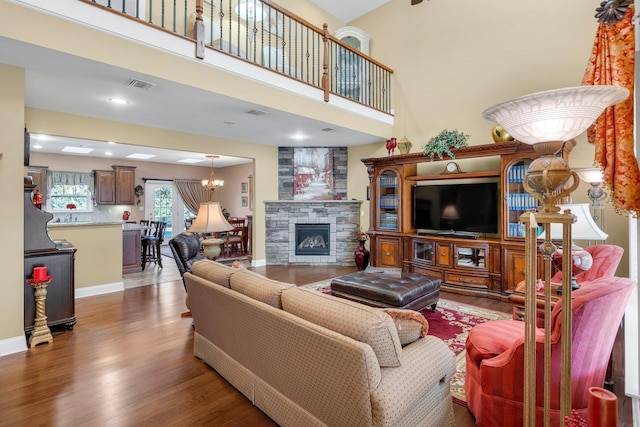 living room with hardwood / wood-style floors, a stone fireplace, a high ceiling, and a chandelier