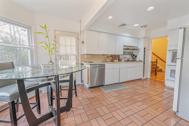 kitchen with decorative backsplash, white appliances, crown molding, white cabinetry, and range hood