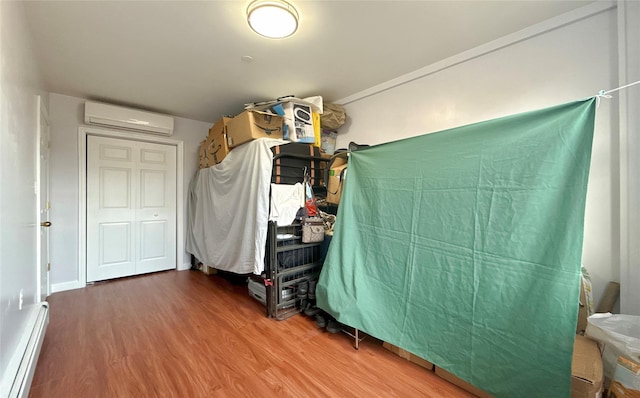 bedroom featuring a wall mounted air conditioner, wood-type flooring, and a baseboard heating unit