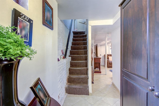 stairs with tile patterned floors and brick wall