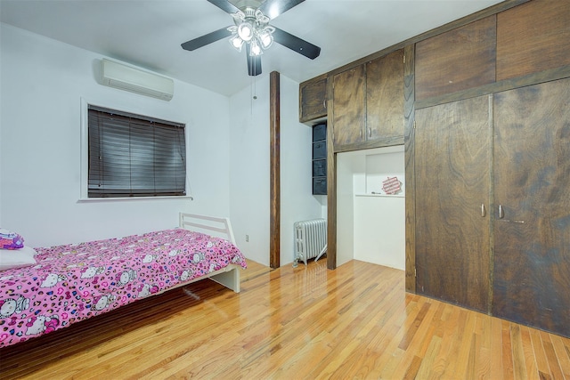 bedroom with light hardwood / wood-style floors, a wall unit AC, radiator, and ceiling fan