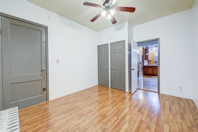 unfurnished bedroom featuring multiple closets, ceiling fan, and light hardwood / wood-style flooring