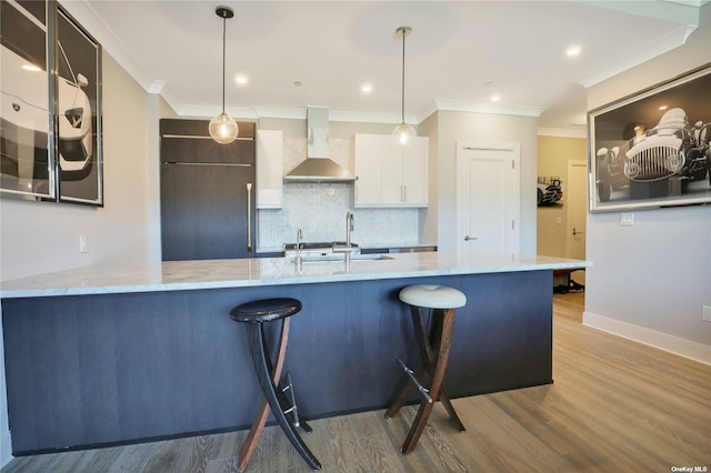 kitchen with wall chimney range hood, built in refrigerator, light wood-type flooring, decorative light fixtures, and white cabinetry