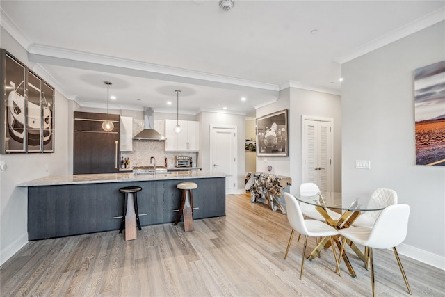 kitchen featuring wall chimney range hood, paneled refrigerator, decorative light fixtures, light hardwood / wood-style floors, and white cabinetry