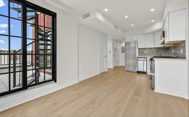 kitchen with decorative backsplash, white cabinetry, stainless steel appliances, and light hardwood / wood-style floors