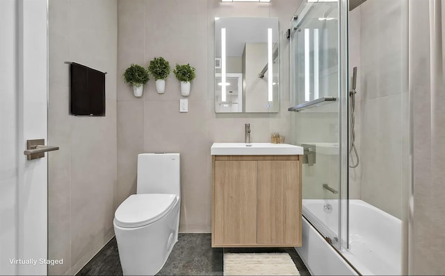 full bathroom with shower / bath combination with glass door, vanity, tile walls, and toilet