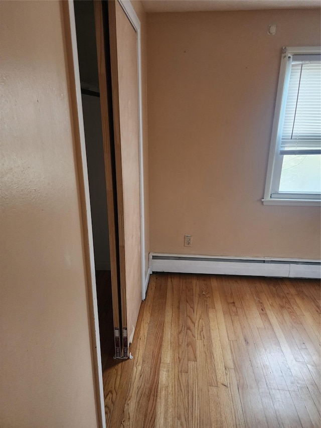 unfurnished bedroom with light hardwood / wood-style floors, a closet, and a baseboard heating unit