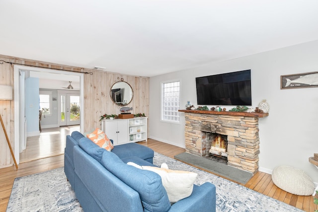 living room featuring light hardwood / wood-style floors, a stone fireplace, and wood walls