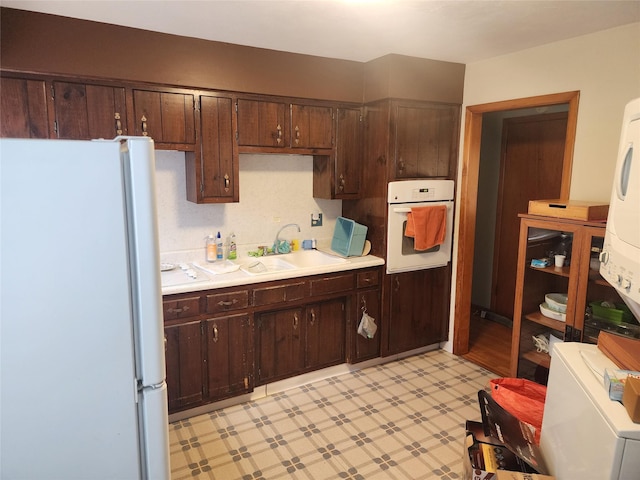 kitchen with white appliances, dark brown cabinetry, and sink