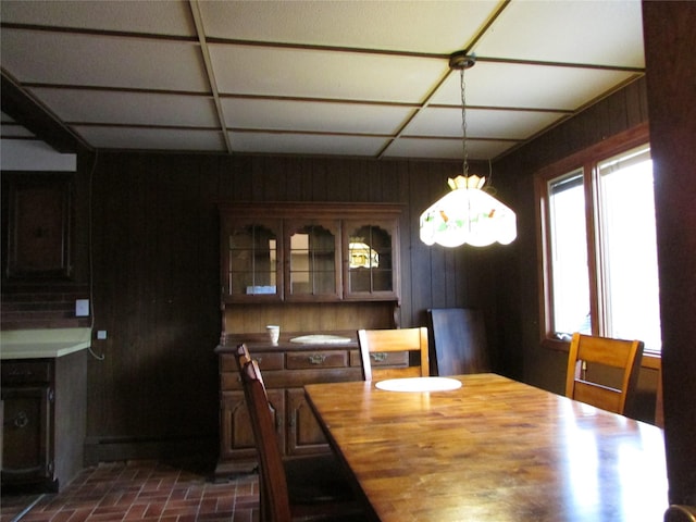 dining space featuring a paneled ceiling, wood walls, and an inviting chandelier