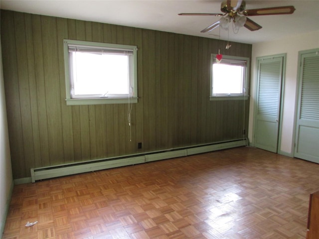 empty room with wood walls, light parquet flooring, ceiling fan, and a baseboard radiator