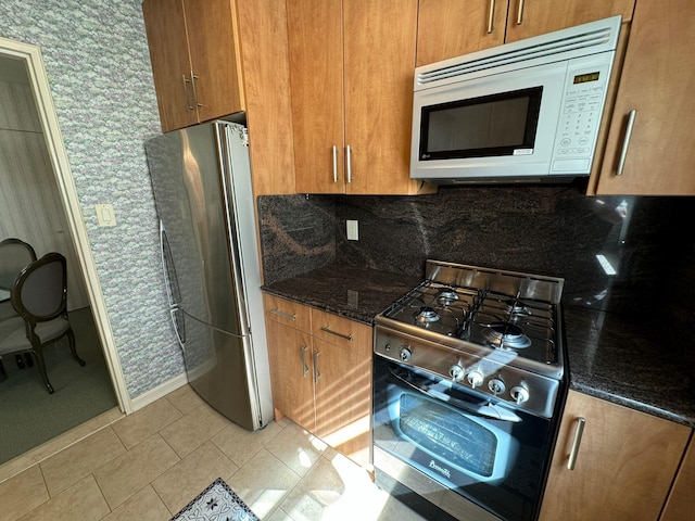 kitchen featuring appliances with stainless steel finishes, tasteful backsplash, light tile patterned floors, and dark stone counters