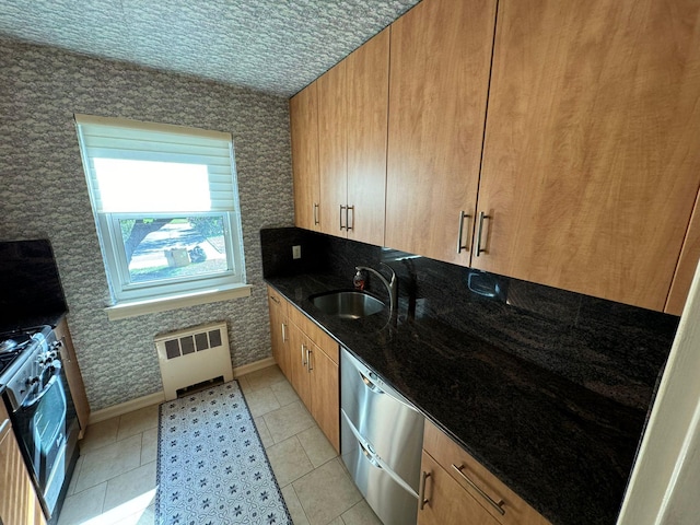 kitchen featuring radiator, sink, dark stone counters, light tile patterned floors, and appliances with stainless steel finishes