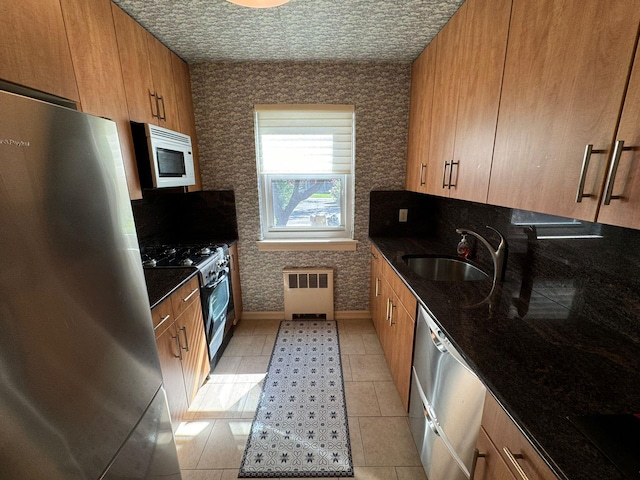 kitchen featuring radiator, sink, stainless steel appliances, dark stone counters, and light tile patterned floors