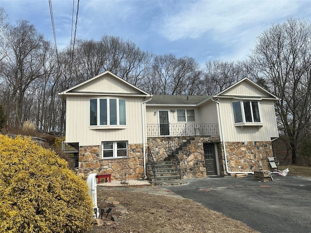 view of front of home with aphalt driveway, stone siding, an attached garage, and stairs