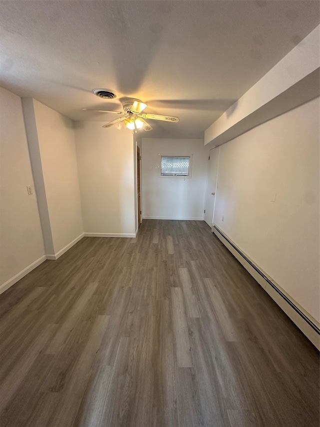 interior space featuring wood finished floors, visible vents, baseboards, ceiling fan, and a baseboard heating unit