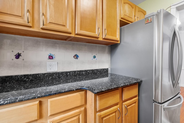 kitchen with dark stone countertops, stainless steel fridge, and decorative backsplash