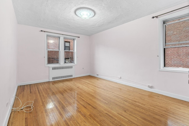 spare room with hardwood / wood-style flooring, plenty of natural light, radiator heating unit, and a textured ceiling