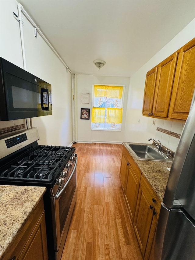 kitchen with sink, light hardwood / wood-style floors, light stone counters, and stainless steel gas range