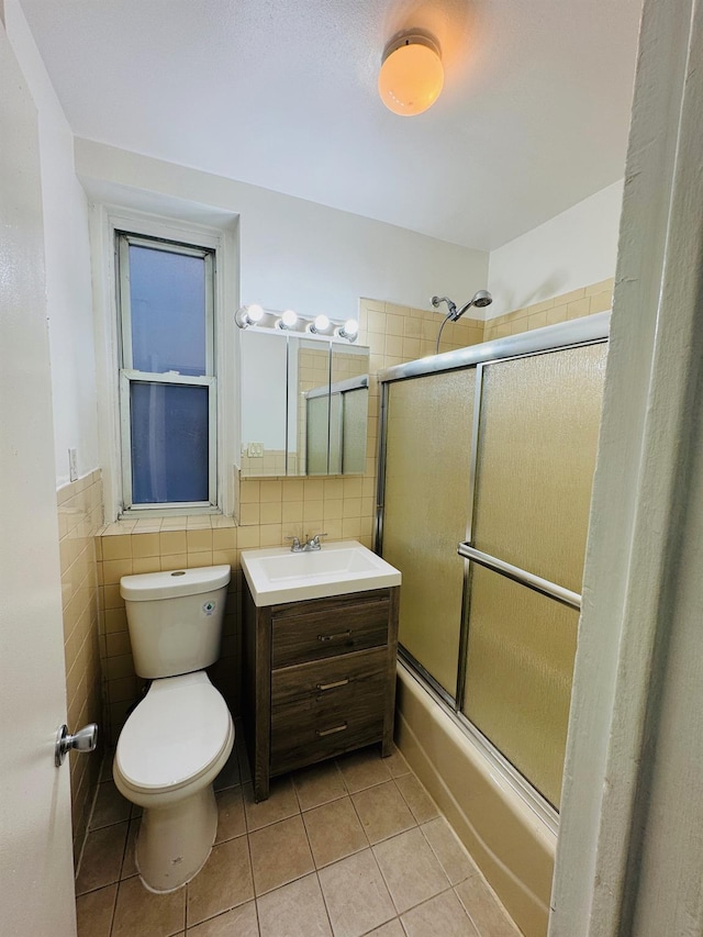 full bathroom with combined bath / shower with glass door, vanity, tile walls, tile patterned flooring, and toilet