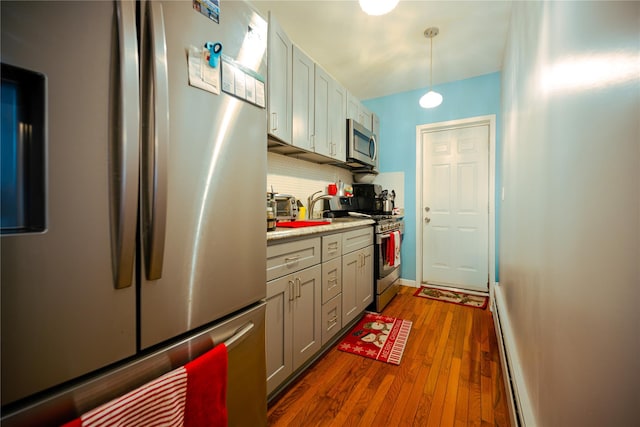 kitchen featuring dark wood-type flooring, stainless steel appliances, a baseboard radiator, pendant lighting, and decorative backsplash