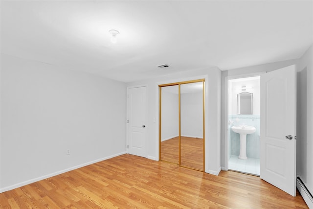 unfurnished bedroom featuring ensuite bathroom, a baseboard heating unit, wood-type flooring, and a closet