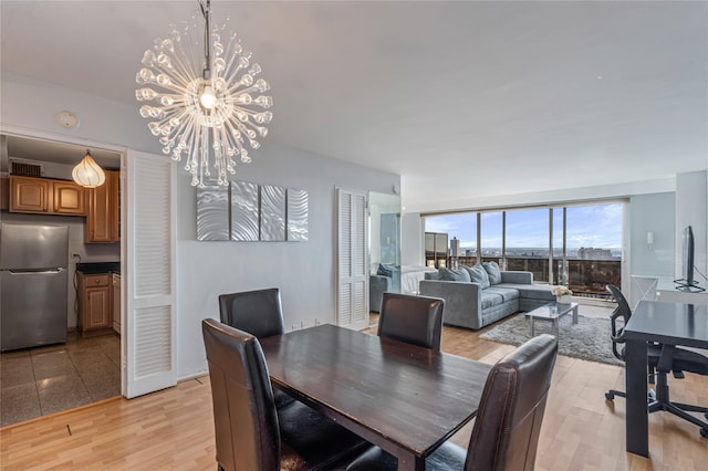 dining room featuring an inviting chandelier, a wall of windows, and light wood-type flooring