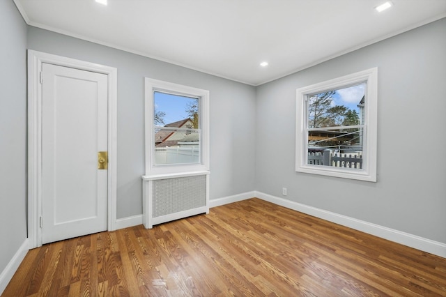 unfurnished room with a wealth of natural light, radiator heating unit, crown molding, and hardwood / wood-style flooring