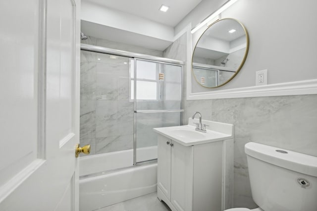 full bathroom with vanity, toilet, bath / shower combo with glass door, and tile walls