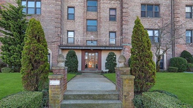 view of exterior entry with a lawn and a balcony