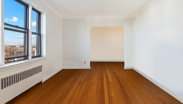 empty room with hardwood / wood-style flooring, radiator heating unit, and crown molding