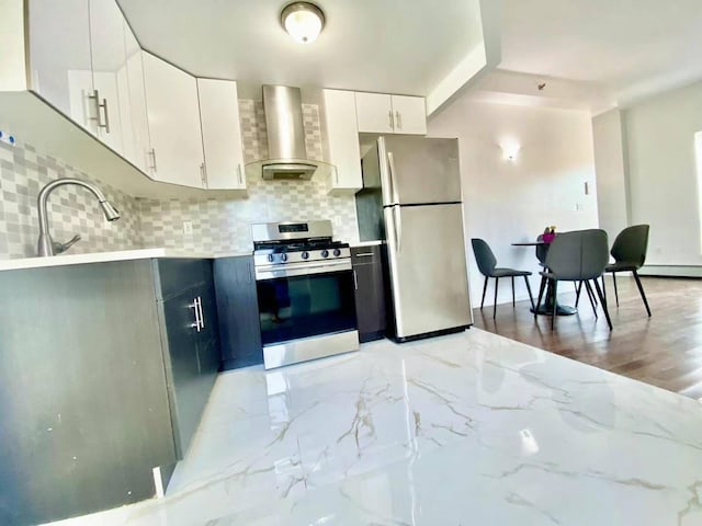 kitchen featuring appliances with stainless steel finishes, light wood-type flooring, backsplash, wall chimney range hood, and white cabinetry