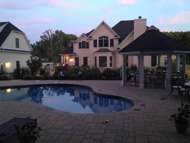 pool at dusk with a gazebo and a patio area