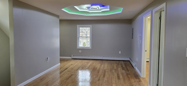 spare room featuring a tray ceiling, a baseboard radiator, and light wood-type flooring