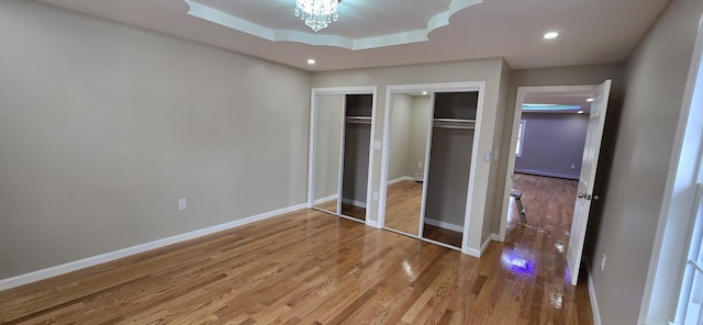 unfurnished bedroom with hardwood / wood-style floors, a baseboard heating unit, two closets, and a chandelier