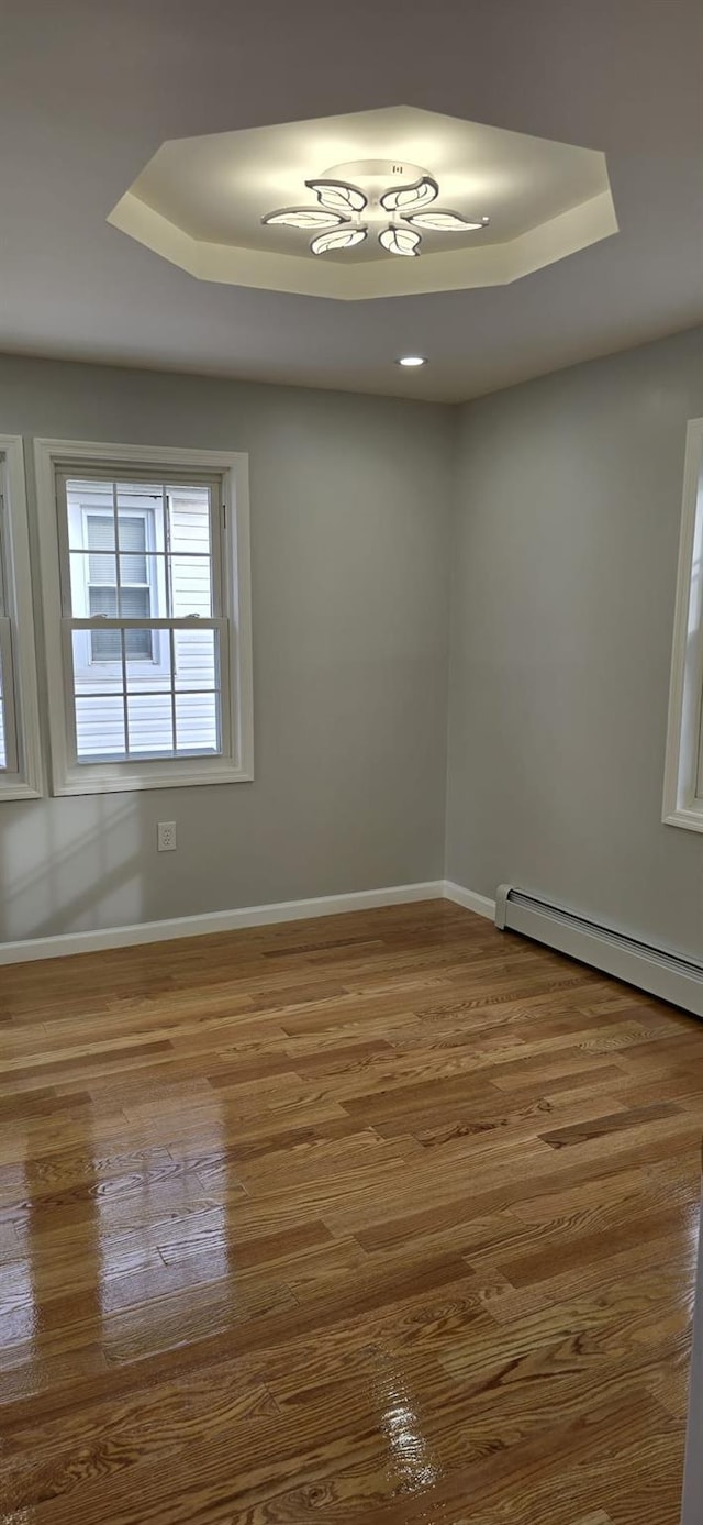 empty room with hardwood / wood-style flooring, a raised ceiling, and a baseboard radiator