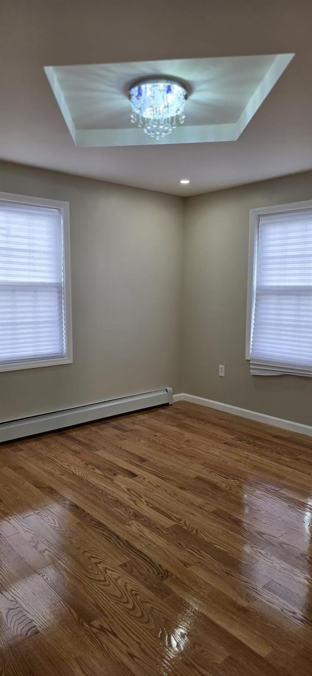 empty room featuring baseboard heating, plenty of natural light, and hardwood / wood-style flooring