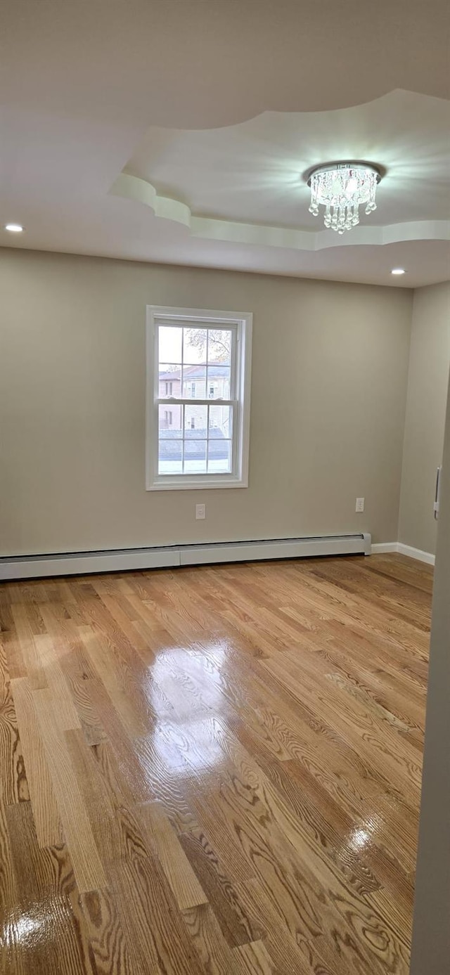 unfurnished room featuring light hardwood / wood-style flooring, a baseboard radiator, and a notable chandelier