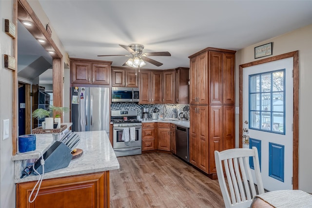 kitchen with ceiling fan, light stone countertops, light wood-type flooring, tasteful backsplash, and stainless steel appliances