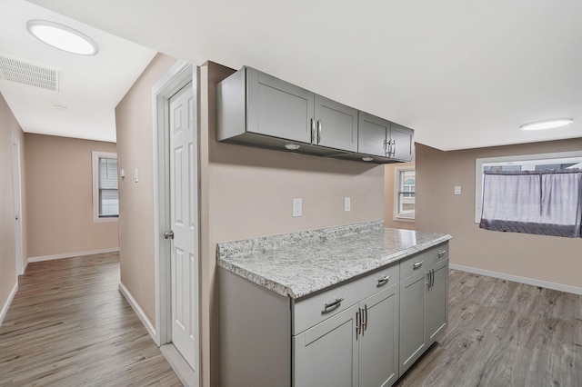 kitchen with light stone countertops, light wood-type flooring, and gray cabinetry