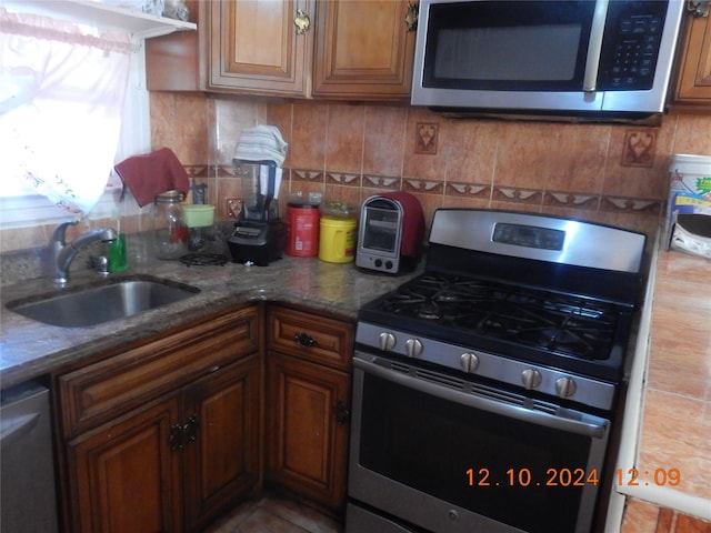 kitchen featuring backsplash, dark stone countertops, sink, and stainless steel appliances