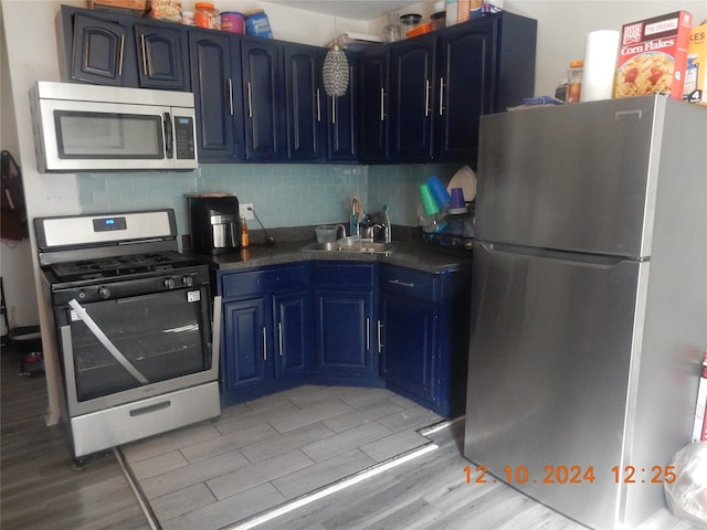 kitchen featuring sink, blue cabinets, backsplash, appliances with stainless steel finishes, and light wood-type flooring