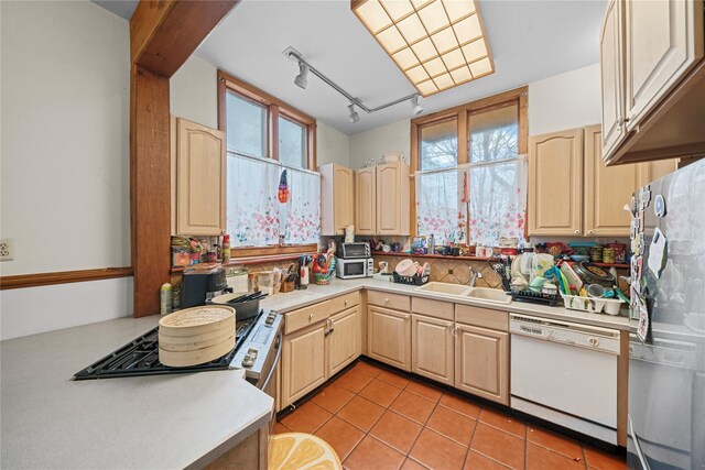 kitchen with white dishwasher, light tile patterned floors, sink, and light brown cabinetry